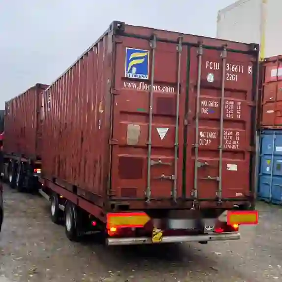 Container 20 pieds d’occasion rouge vu de trois-quarts arrière sur remorque, traces d’usage visibles